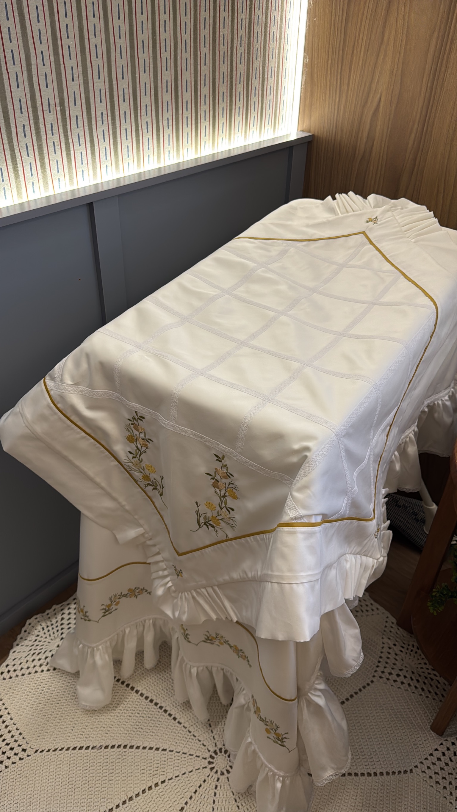 Colcha de berço branca com bordado floral dourado, faixa e babado de cetim com renda
